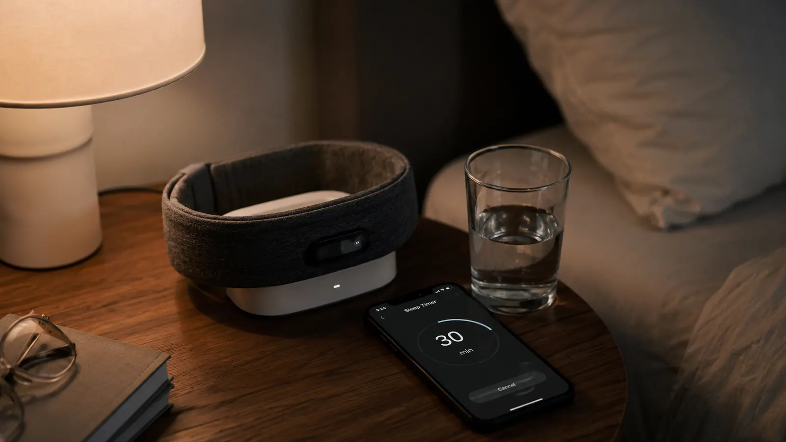 Nightstand scene with a charging headband, phone showing a sleep timer, and a glass of water