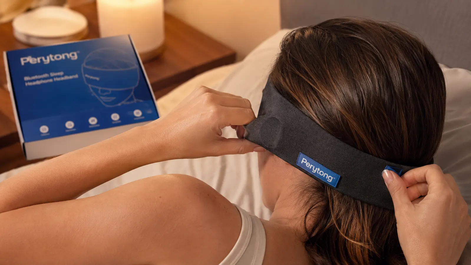 Hand adjusting the Perytong Bluetooth headband over the ears before bed, showing the thin flat speaker sitting flush against the fabric